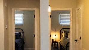Un pasillo estrecho con suelo de madera que conduce a dos dormitorios, cada uno con cama y ventana.