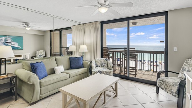 Un vaste espace de vie comprenant un canapé, des fauteuils, une table basse et un balcon offrant une vue sur la plage.