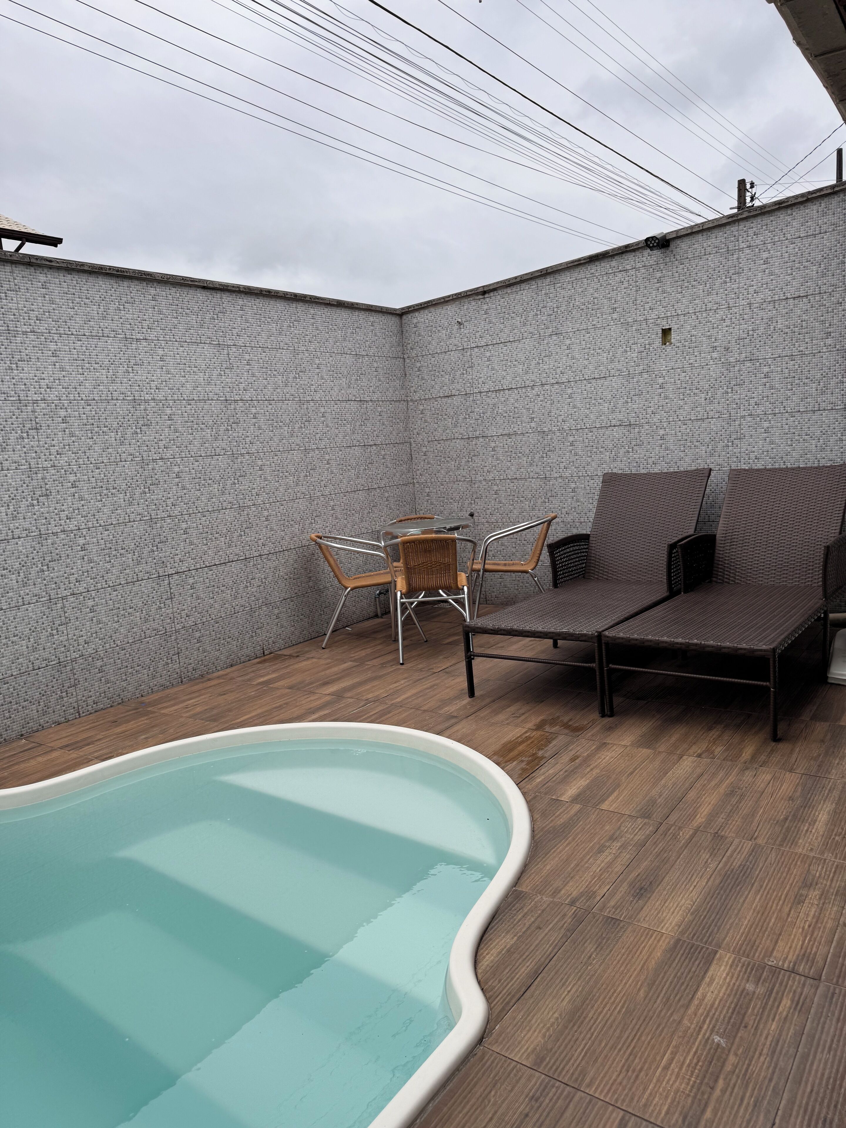 Une piscine entourée d’une terrasse en bois, de chaises en osier et d’une table.