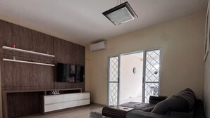 Una sala de estar moderna con un sofá gris, un televisor de pantalla plana, estantes empotrados y un ventanal corredero que da a un balcón.