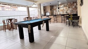 Una mesa de billar con sillas, una zona de bar con taburetes y un suelo de baldosas.