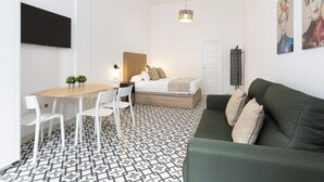 A modern, well-lit room with a bed, a green sofa, a dining table with chairs, and a TV mounted on the wall. - Picasuss Loft Close Beach & Promenade (Málaga)