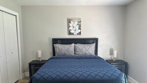 Une chambre à coucher comprenant un lit, deux tables de chevet, une commode, une porte et un tableau accroché au mur.