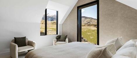 Un dormitorio con una cama grande, dos sillones y vistas a un paisaje montañoso a través de un amplio ventanal.