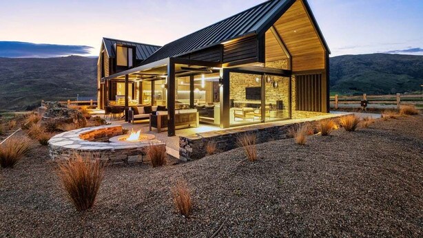 Een modern huis met een stenen openhaard, grote ramen en uitzicht op het omliggende landschap.