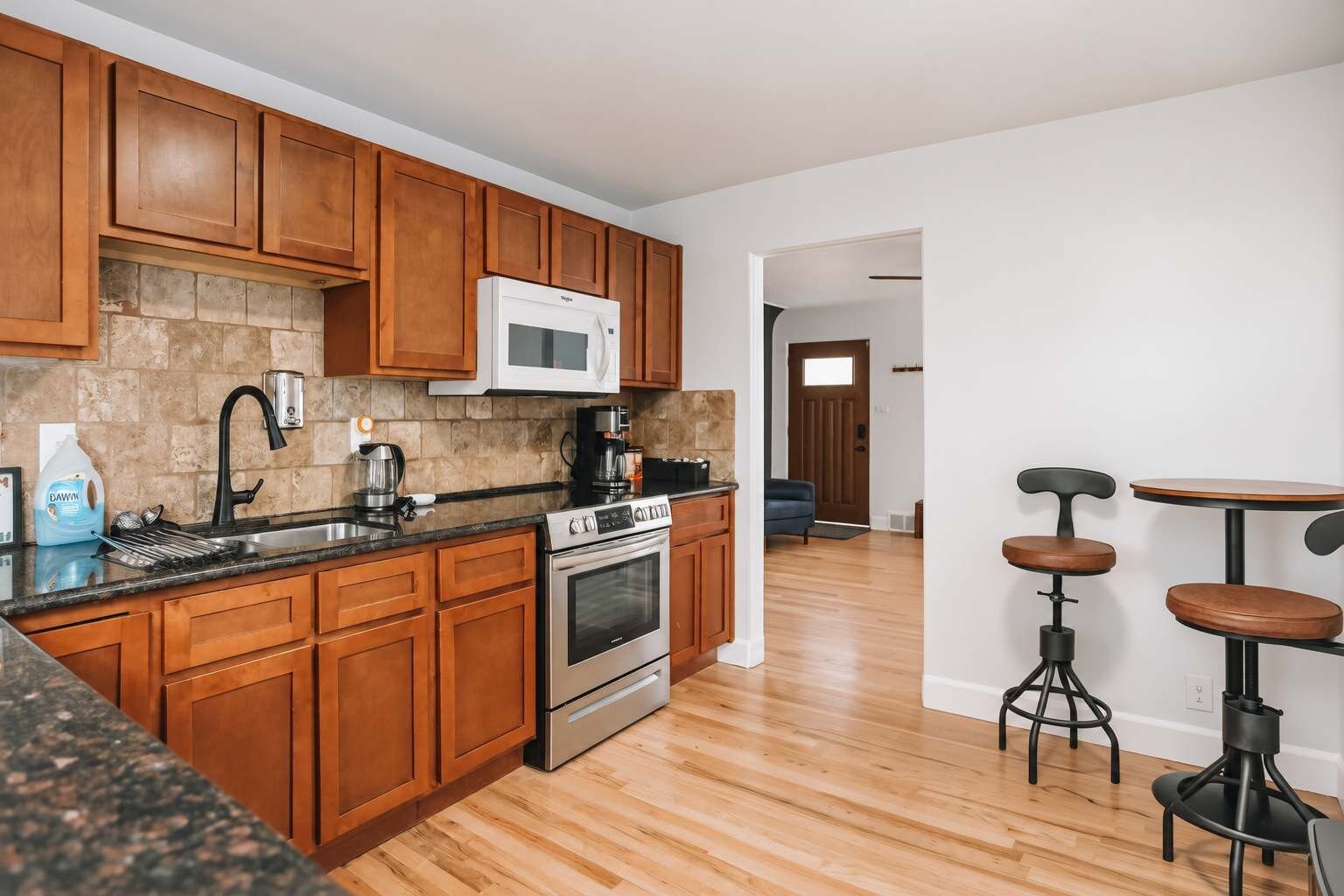 A kitchen with wooden cabinets, a stainless steel oven, a microwave, and a coffee maker. There is a wooden dining table with stools.