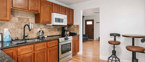 A kitchen with wooden cabinets, a stainless steel oven, a microwave, and a coffee maker. There is a wooden dining table with stools.