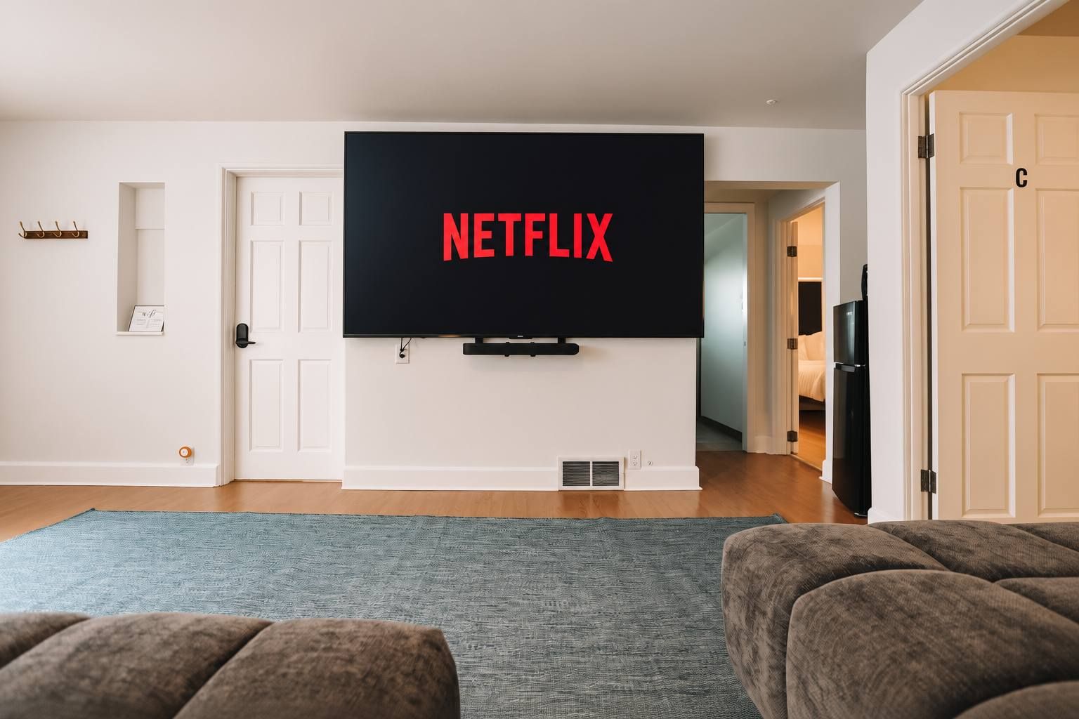 A living room with a flat-screen TV mounted on the wall displaying 'NETFLIX' in red letters, a gray area rug, and two brown couches.