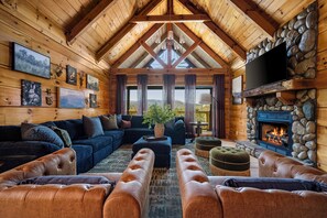 A log cabin interior with a fireplace, leather sofas, a television, and artwork on the walls. - Foxhaven Ridge: Mtn Views • Sauna • Hot Tub • Cold Plunge - Lux Family Retreat (Sevierville)