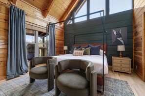 A wooden cabin bedroom with a bed, two armchairs, a nightstand, and a window with curtains. - Foxhaven Ridge: Mtn Views • Sauna • Hot Tub • Cold Plunge - Lux Family Retreat (Sevierville)