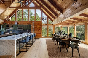 A spacious wooden cabin with a large dining area, kitchen, and a view of the surrounding forest. - Foxhaven Ridge: Mtn Views • Sauna • Hot Tub • Cold Plunge - Lux Family Retreat (Sevierville)