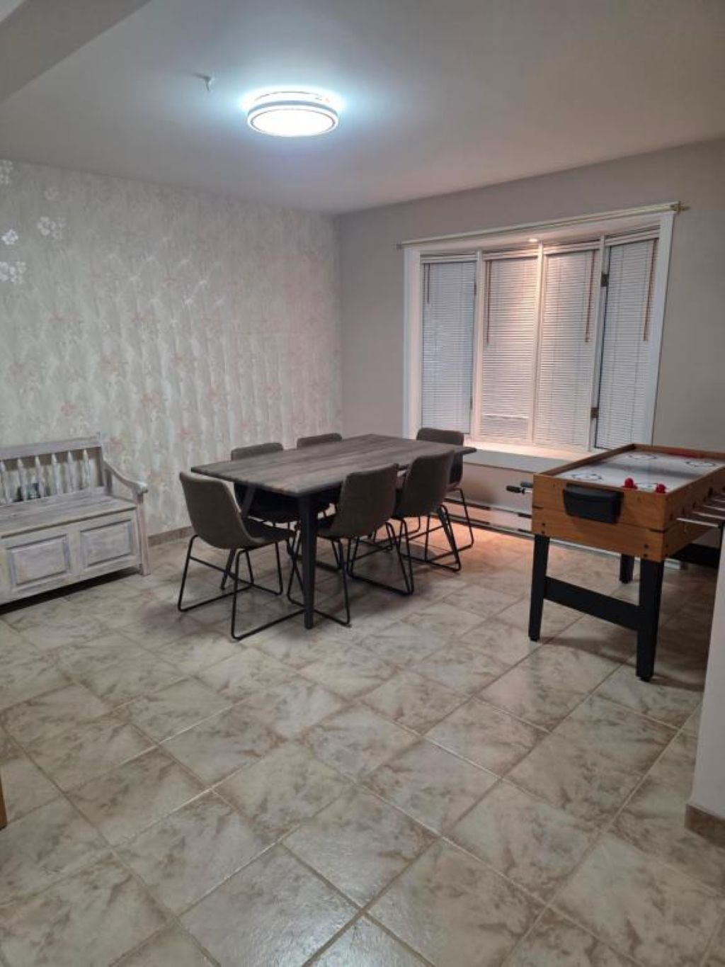 Un área de comedor con una mesa rectangular rodeada de sillas, una mesa de fútbol de mesa y un sofá.