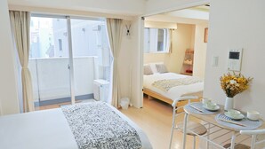 Habitación de hotel con una cama grande, una mesita con juego de té, un jarrón con flores y vistas a edificios a través de la ventana.