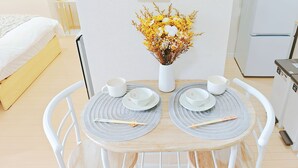 Una mesa de comedor ordenada con dos sillas blancas, un jarrón de flores amarillas y tazas y fuentes blancas a juego sobre individuales.