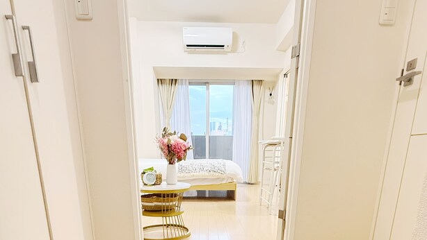 Habitación de hotel con cama, mesita de noche, una pequeña mesa con un reloj y ventana con cortinas.