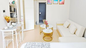 Una sala de estar moderna con un sofá blanco, una mesa de comedor con sillas, una pequeña cocina y una puerta que da a otra habitación.