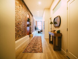 A hallway with a brick wall, a wooden floor, a rug, a console table with lamps, and a mirror. - Historic 2BR suite in Halifax w/ Free Parking (Halifax)