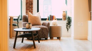 Ein gemütliches Wohnzimmer mit Sofa, Sessel und Hocker, einem kleinen runden Tisch und einem Fenster mit Aussicht.