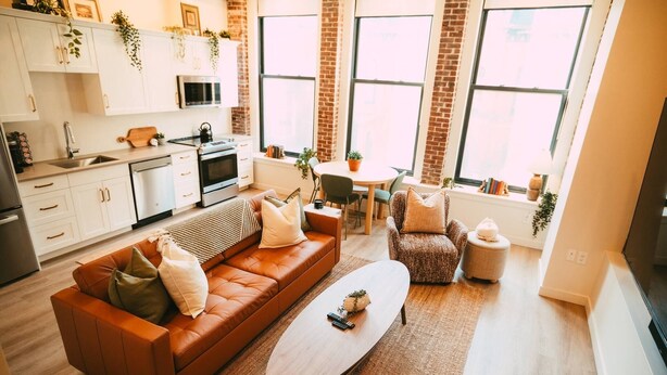 Eine moderne Küche mit weißen Schränken, ein Essbereich mit einem runden Tisch und ein Wohnzimmer mit einem braunen Sofa und einem Couchtisch.