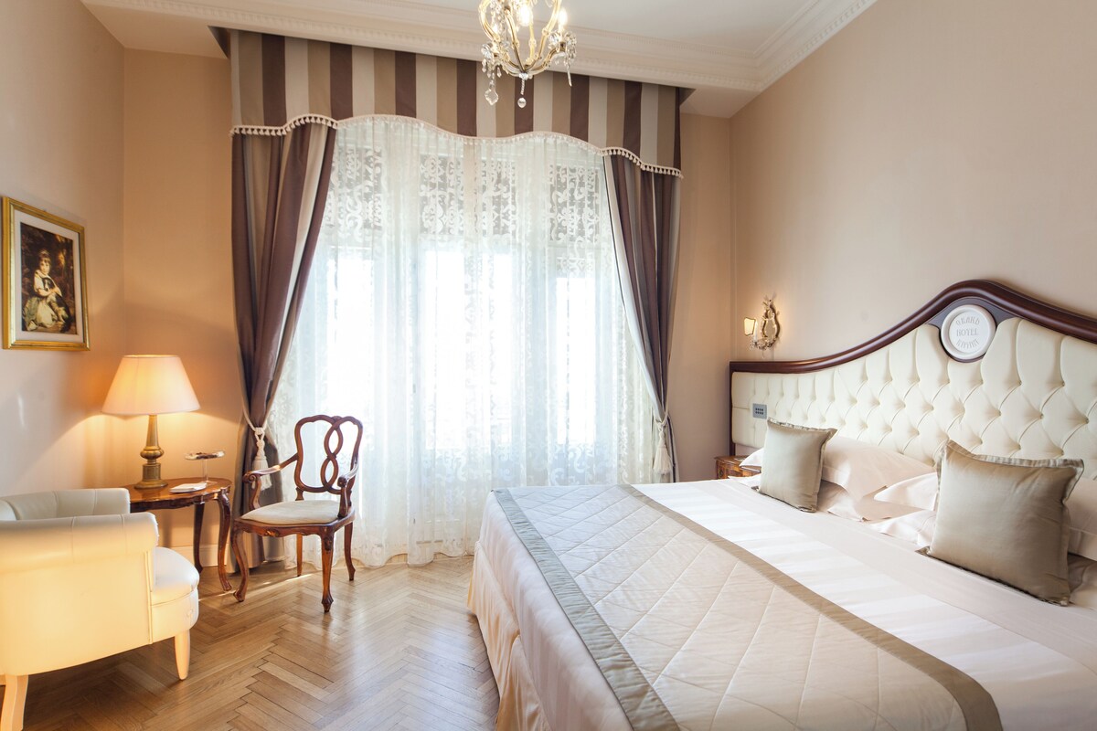 A hotel room with a large bed, a chair, a lamp, and a painting on the wall.