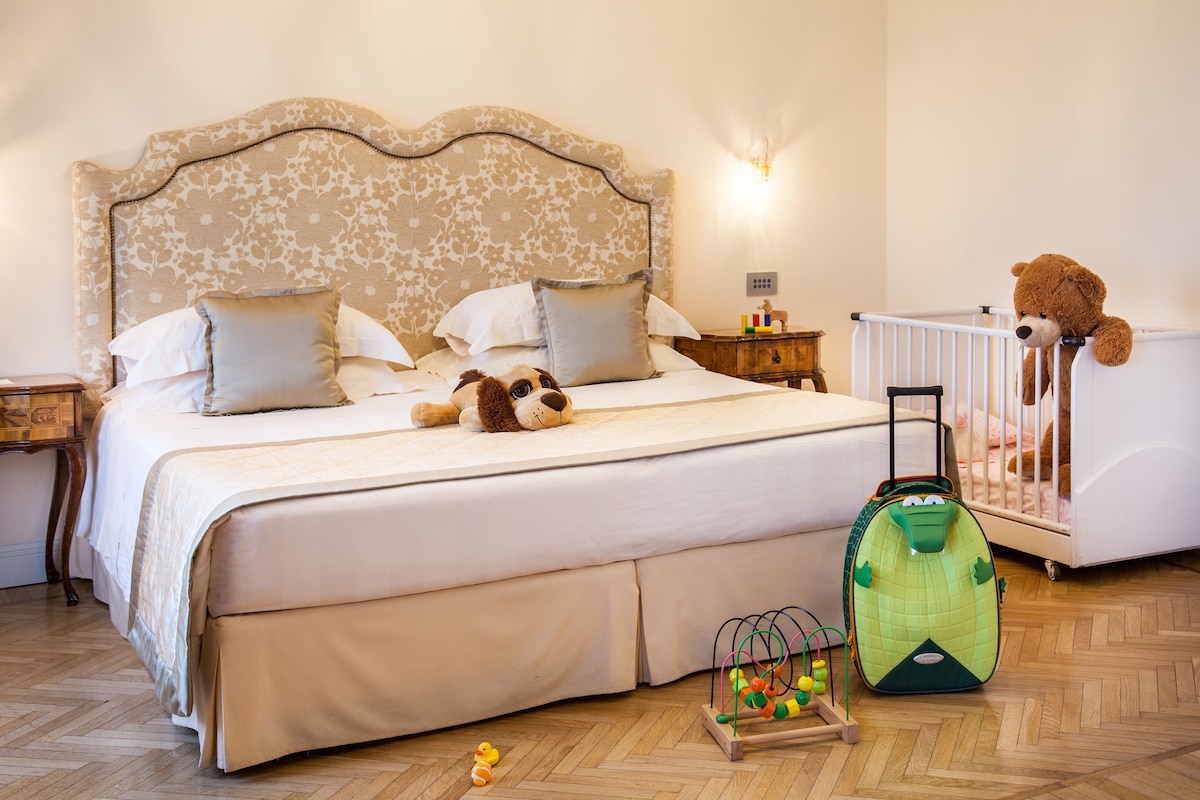 A bedroom with a bed, pillows, a nightstand, a crib, a teddy bear, and a toy.