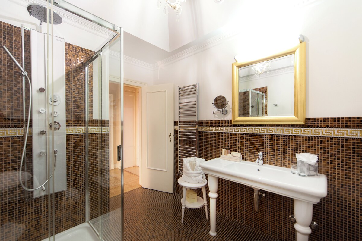 A bathroom with a glass-enclosed shower, a white sink with two mirrors, and a tiled backsplash.