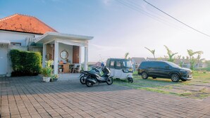 A residential area with a paved driveway, a motorcycle, a tuk-tuk, and a car parked in front of a house with a tiled roof and a porch. - Lavanya Villas Beautiful 1-bedroom Private Pool Villa (Ubud)