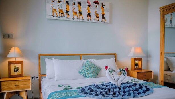 Ein ordentlich bezogenes Bett mit einer blau-weißen Karodecke, zwei Nachttischlampen, einem gerahmten Bild auf dem Nachttisch und einem Wandbild über dem Bett.