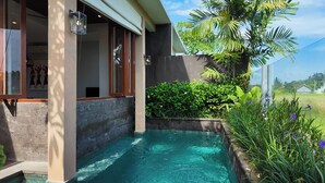 A modern pool area with a clear blue pool, a stone wall, and lush greenery including palm trees and flowering plants. - Lavanya Villas Beautiful 1-bedroom Private Pool Villa (Ubud)