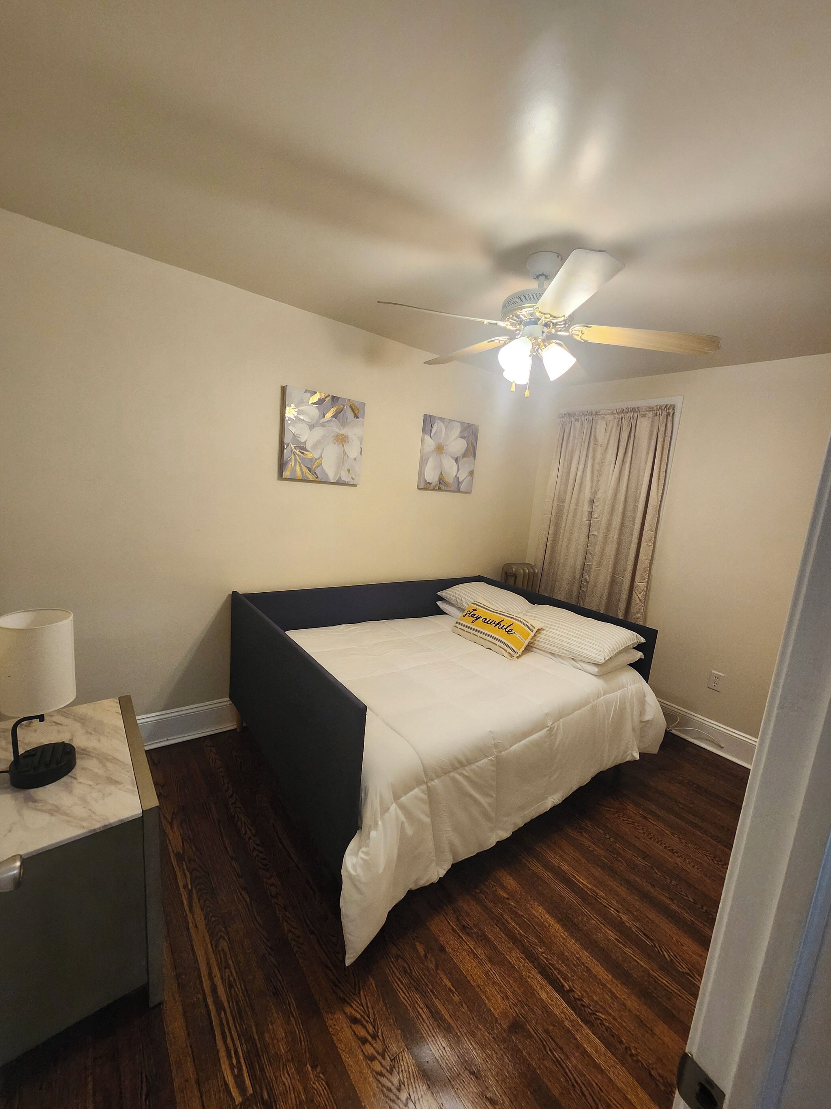 Ein Schlafzimmer mit einem Bett, einem Nachttisch, einem Deckenventilator und zwei an der Wand befestigten Bildern.