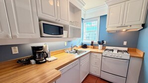 Een kleine keuken met witte kastjes, een magnetron, een gasfornuis en een spoelbak.