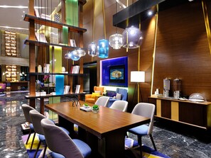 A modern hotel lobby with a wooden reception desk, seating area, and a TV screen.