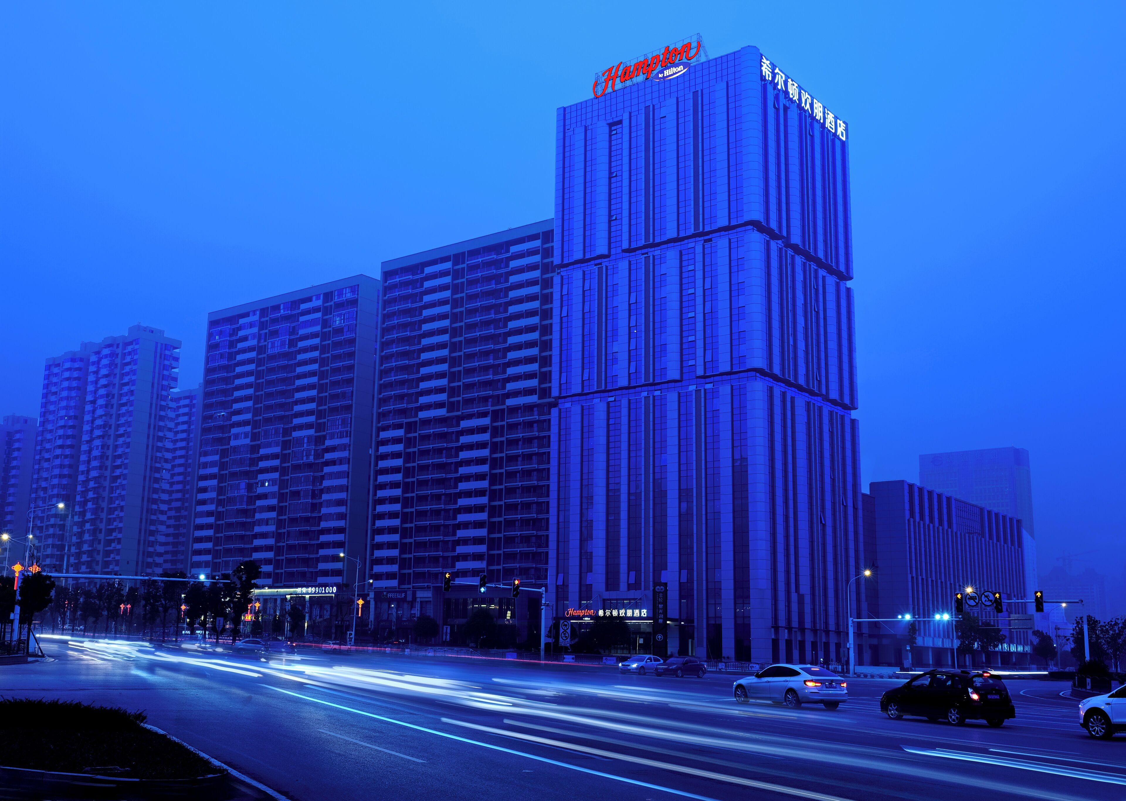 A high-rise hotel with a prominent 'Hampton' sign, multiple floors, and a modern architectural design.