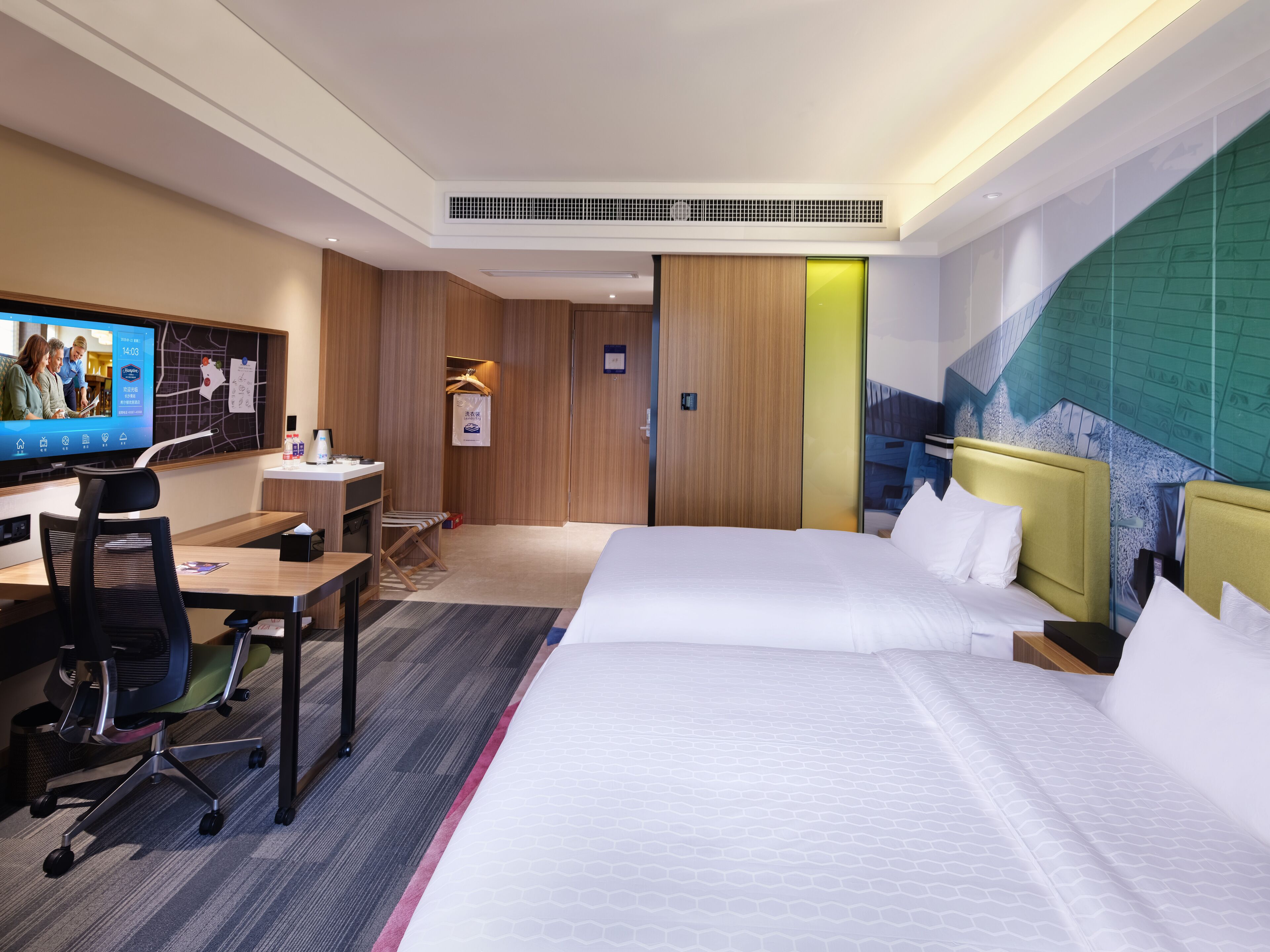 A hotel room with a bed, desk, chair, television, and a wall with a map.