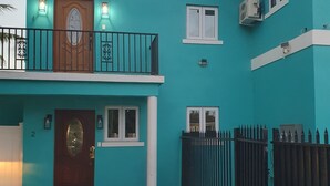 A two-story building with a teal exterior, a wooden front door, and a balcony. - Enjoyable 1-bedroom apartment with AC in welcoming Nassau (Nassau)