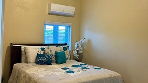 A bedroom with a bed, a ceiling fan, an air conditioning unit, a window, and a vase with flowers. - Enjoyable 1-bedroom apartment with AC in welcoming Nassau (Nassau)