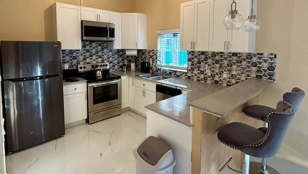 A modern kitchen with white cabinets, stainless steel appliances, a marble countertop, and bar stools. - Enjoyable 1-bedroom apartment with AC in welcoming Nassau (Nassau)