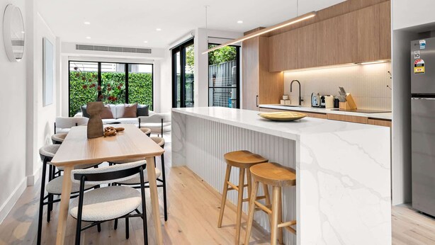 A modern kitchen with a marble countertop, wooden cabinets, and a stainless steel refrigerator. - Stylish 3-Bed Home Near South Melbourne Market (South Melbourne)