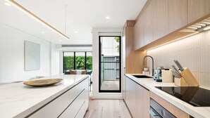 A modern kitchen with a central island, built-in appliances, and a view to a green outdoor area. - Stylish 3-Bed Home Near South Melbourne Market (South Melbourne)