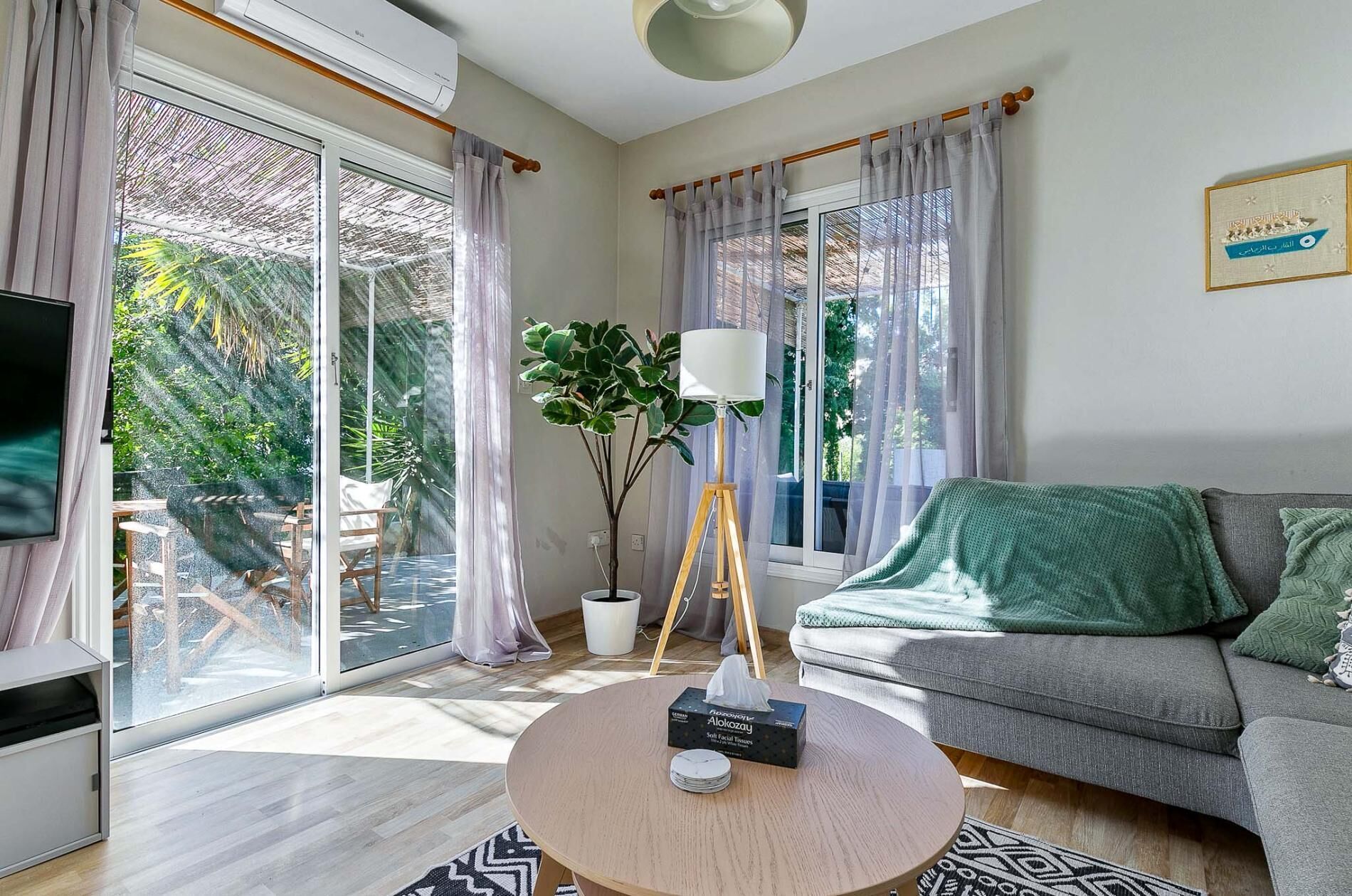 Un salon moderne avec un canapé gris, une table basse ronde sur laquelle se trouve une boîte à mouchoirs, un lampadaire et un téléviseur placé à gauche.
