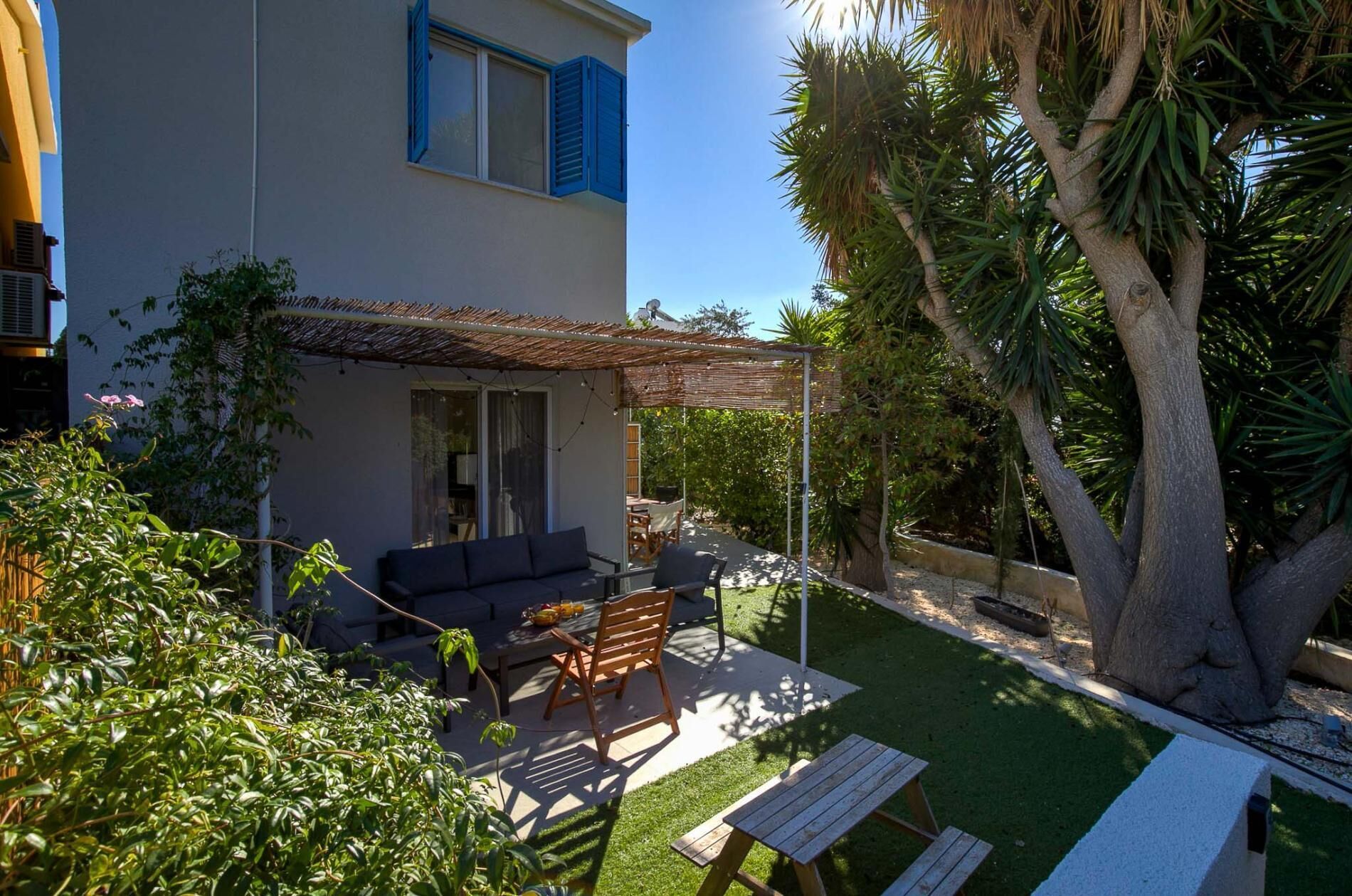 A covered outdoor seating area with a sofa and chairs, a table, and a large tree.