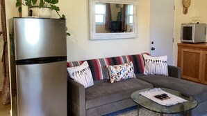 A compact living space with a sofa, a glass coffee table, a refrigerator, a microwave, and a mirror. - Cozy 1-bedroom studio barn cottage in tranquil Winters (Winters)