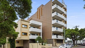 A multi-story residential building with balconies, a parking area, and a street view. - Ground Floor One-Bed with Courtyard Access (Strathfield)