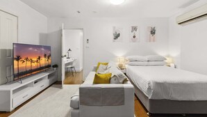 A modern bedroom with a bed, bedside table, lamp, and a TV displaying a sunset scene. - Ground Floor One-Bed with Courtyard Access (Strathfield)