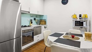 A modern kitchen with stainless steel appliances, a dining area with a checkered tablecloth, and a yellow kettle on a shelf. - Ground Floor One-Bed with Courtyard Access (Strathfield)