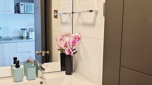 A modern bathroom with a white sink, wooden cabinets, a mirror, and a vase with pink flowers. - Moderno impecable Cercano a terminales (Temuco)