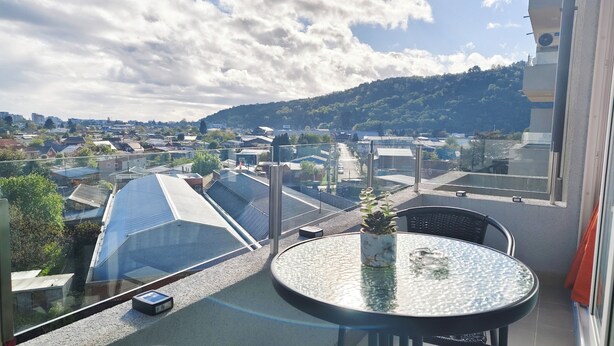 A balcony with a glass table and chairs, overlooking a cityscape with buildings and a hill. - Moderno impecable Cercano a terminales (Temuco)