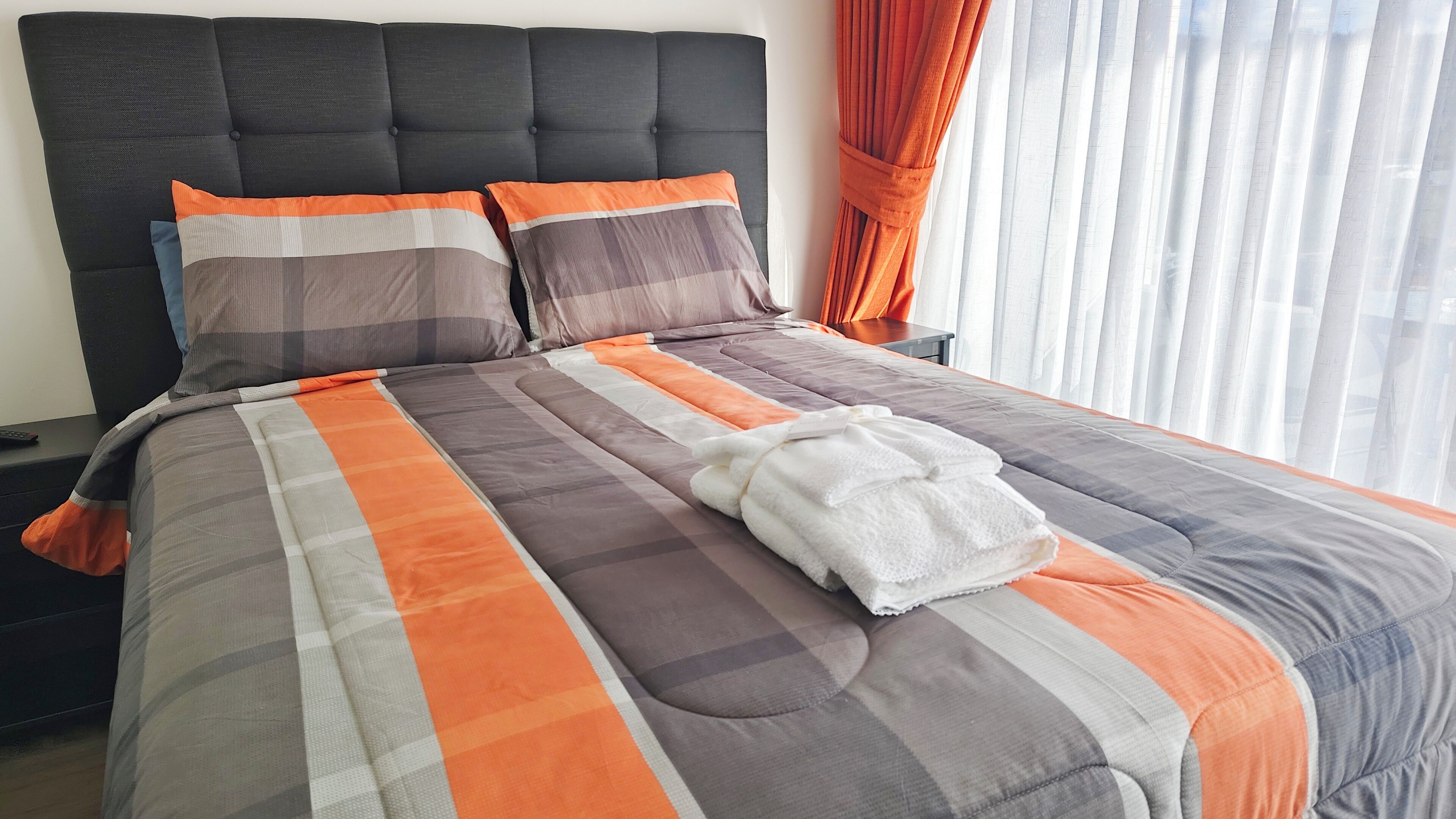 Una cama bien tendida con una colcha a rayas, dos almohadas y una toalla blanca.