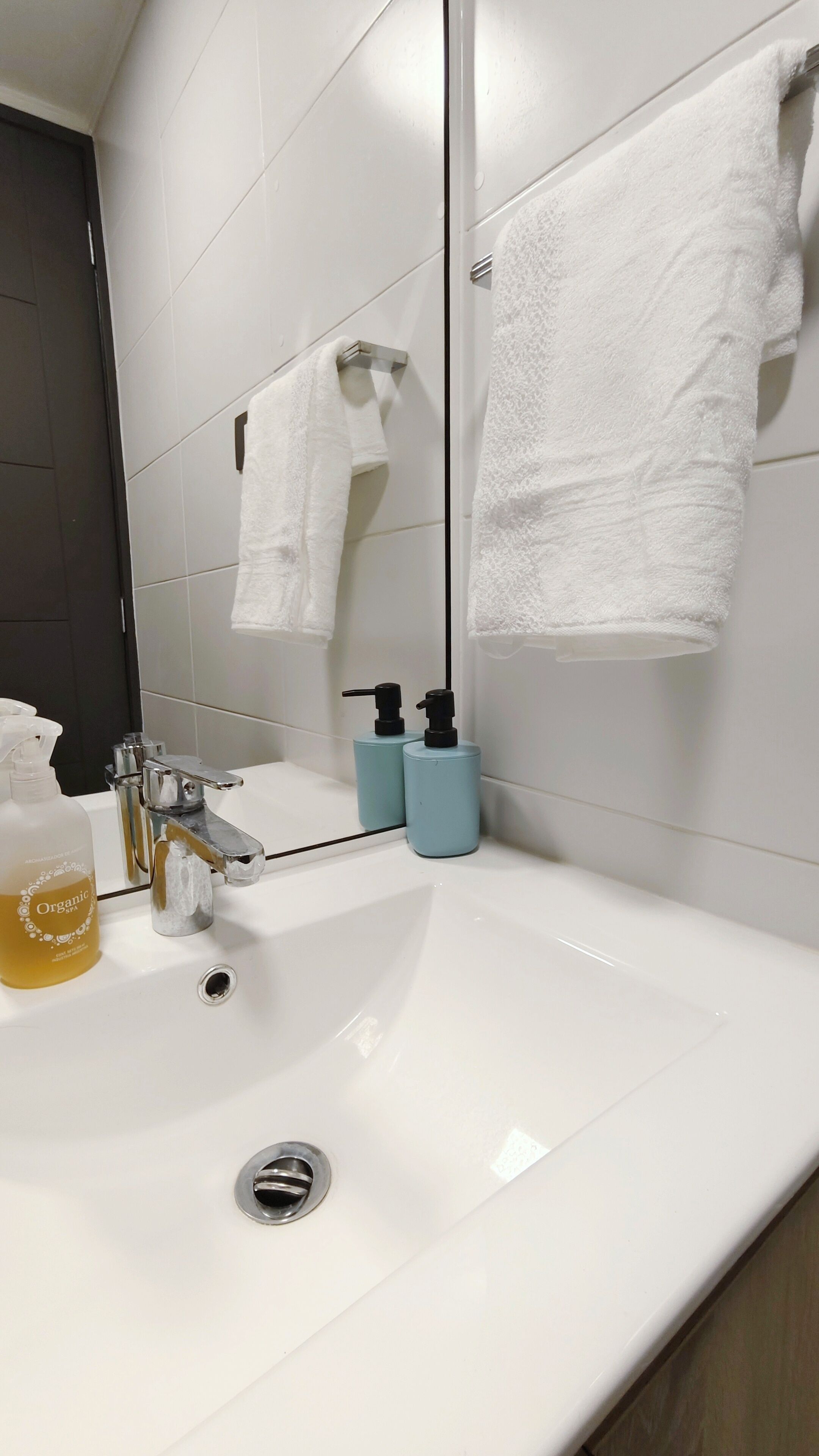 A bathroom with a white sink, two soap dispensers, a bottle of organic spa soap, a mirror, and two white towels hanging on a rack.