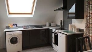 A compact kitchen with a washing machine, a stove, a sink, and a window above the countertop. - Binnian View Apartment - Sleeps 4 (Newry)